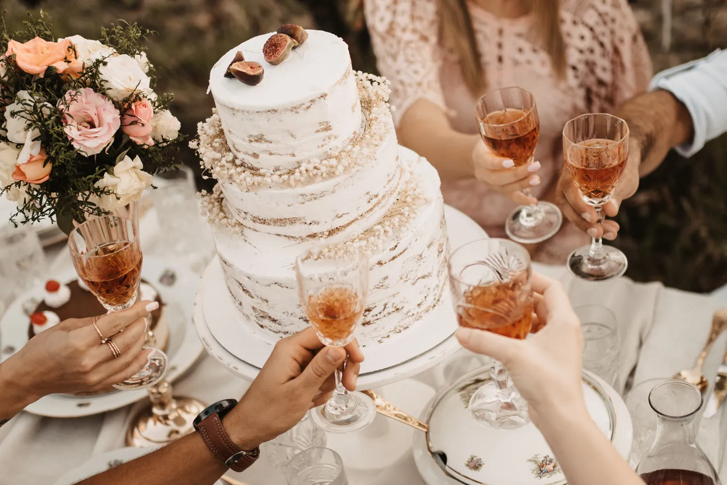 closeup wedding table with cake people holding glasses with beverages